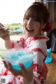 A woman in a red and white kimono holding a bowl of blue liquid.