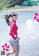 A woman in a pink shirt and blue shorts running on the beach.