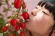 A woman is smelling a bunch of tomatoes on a plant.