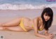 A woman in a yellow bikini laying on the beach.