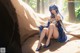 A woman in a blue dress sitting on a rock.