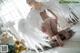 A woman in a white lingerie with angel wings sitting on the floor.