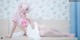 A woman in a pink and white outfit sitting on a bed.